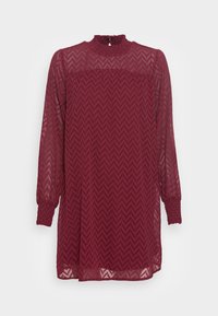 Bordeauxrode jurk van doorschijnende stof met een chevronpatroon, een hoge gerimpelde hals en lange mouwen met gerimpelde manchetten. Voorzien van een keyhole-sluiting aan de achterkant.