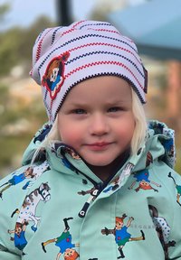 Raidallinen valkoinen ja punainen neulottu hattu, jossa on sarjakuvatyttökuva; vihreä takki, jossa on toistuvia lapsi- ja hevospainatuksia.