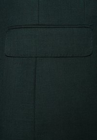 Ciemnozielona tkana tkanina o teksturowym wykończeniu, z prostokątną kieszenią na piersi. Czysty design z minimalistycznym detalem w stębnowaniu.