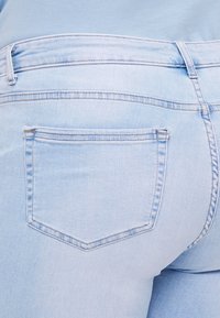 Vaqueros de mezclilla azul claro con un diseño ajustado, que cuentan con un bolsillo trasero, costuras sutiles y una textura suave.