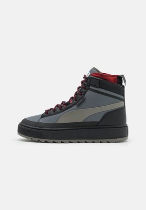 Baskets montantes gris et noir avec des lacets bordeaux, une semelle noire épaisse et un col intérieur rembourré rouge, vues de côté sur fond blanc.