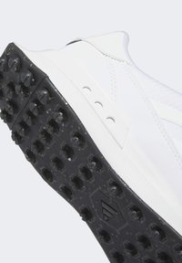 White athletic shoe with textured upper. Black rubber outsole with prominent studs for traction. Features three ventilation holes on the side.