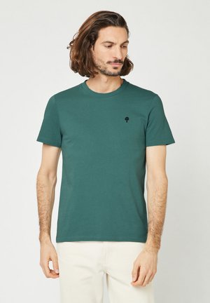 Donkergroen katoenen t-shirt met een ronde halslijn en korte mouwen, voorzien van een klein zwart bomenlogo op de linkerkant van de borst.