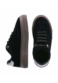 Sneaker in suede nero con una spessa suola in gomma marrone, occhielli rotondi e un accento bianco sul tallone. Presenta una fodera testurizzata per una migliore aderenza.