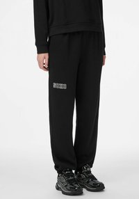Czarne spodnie dresowe ze ściągaczami przy kostkach, z bia�łym nadrukiem "SOHO" na lewej nogawce, wykonane z miękkiego, teksturowanego materiału.