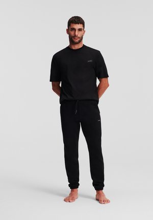 Schwarzes T-Shirt mit kurzen Ärmeln und Rundhalsausschnitt, kombiniert mit schwarzen Jogginghosen mit elastischem Bund und Bündchen. Minimalistisches Design.