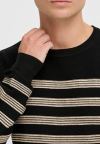 Black sweater with cream horizontal stripes, ribbed neckline, and cuffs. Features a soft, knitted texture and a fitted design.
