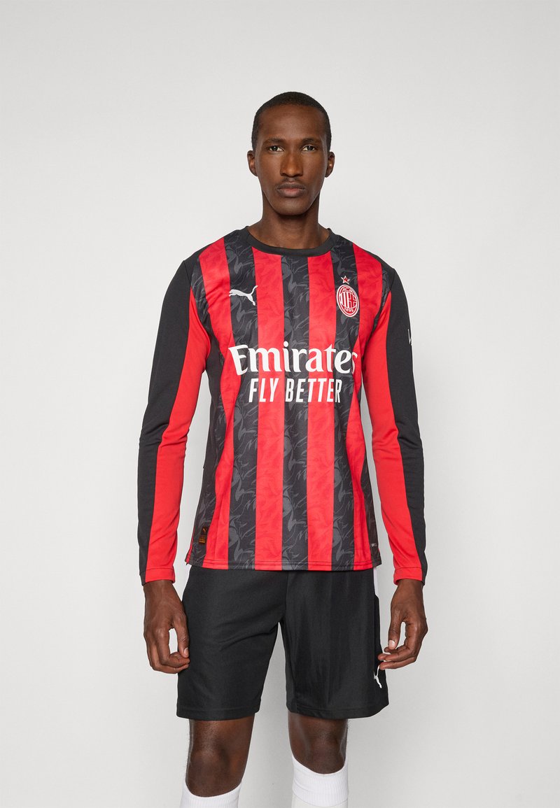 Rød og sort langærmet fodboldtrøje med et struktureret mønster, der har et logo, sponsor tekst og er sat sammen med sorte shorts.