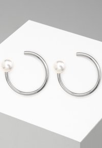 Orecchini a cerchio in argento con un accento di perla. I cerchi sono circolari, lisci al tatto e aperti nella parte inferiore.