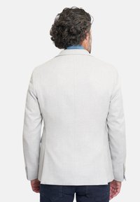 Blazer gris claro con una tela texturizada, solapas de muesca y mangas largas. Presenta dos botones decorativos en los puños, usado sobre una camisa azul.