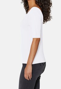 Bílý top bez ramínek s krátkými rukávy, vyrobený z hladké, elastické látky; kombinovaný s černými slim-fit džíny s decentním designem zadní kapsy.
