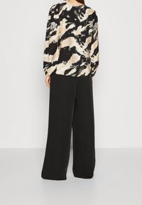 Trykt bluse med lange ærmer, der har et abstrakt mønster i sort, beige og hvid, sammen med vidde bukser i sort.