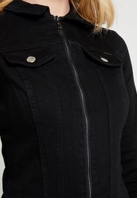 Black denim jacket featuring a zip closure, two chest pockets with snap fasteners, and a structured collar. Smooth texture with subtle stitching.