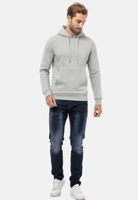 Helle graue Kapuzenjacke mit Kängurutasche und Kordelzügen, getragen mit dunkelblauen Jeans und weißen Sneakers, bietet eine lässige Passform und glatte Textur.