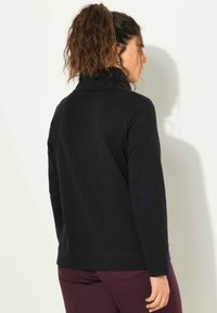 Maglietta nera a maniche lunghe con colletto alto, texture liscia e vestibilità rilassata, abbinata a pantaloni color amaranto. Il design è semplice e funzionale.