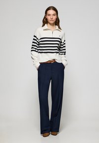 Navy wide-leg trousers paired with a cream sweater featuring navy horizontal stripes and a zip collar. Brown belt accents the outfit.
