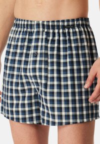 Boxer a quadri blu e bianchi con elastico in vita, chiusura con un solo bottone e tessuto dalla consistenza morbida. Design casual per l'uso quotidiano.
