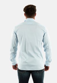 Camisa de manga larga azul claro hecha de tela suave. Presenta puños con botones y un dobladillo redondeado, con un cuello clásico y un diseño de ajuste regular.