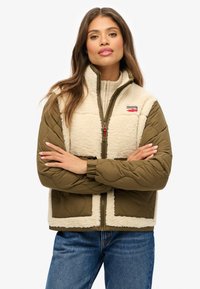 Giacca imbottita in nylon verde oliva, con pannelli in shearling crema, chiusura con zip, colletto rialzato e patch logo rosso a contrasto. Texturizzata e calda.