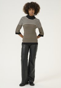 Svart och beige randig stickad topp med hög hals och trekvartslånga ärmar, ihopparad med svarta byxor i konstläder med vida ben och svarta skor.