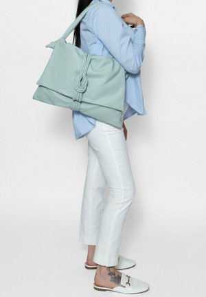 Light green bag made of soft material, featuring a knotted accent, carried over the shoulder with a flat shape.