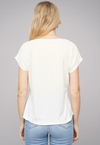 T-shirt blanc à manches courtes avec un ourlet arrondi, fabriqué en tissu doux, affichant une coupe décontractée et une texture subtile, présenté de dos.