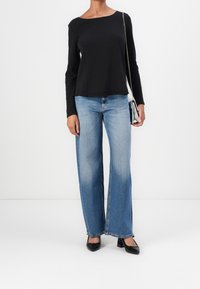 Svart långärmad tröja med vid halsringning, tillsammans med ljusblå vida jeans och svarta klackskor. Inkluderar en liten silverhandväska.