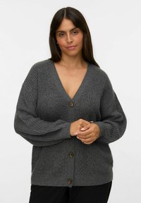Cárdigan gris de punto con un profundo escote en V, mangas oversized y tres botones marrones. Tejido texturizado con detalles en canalé.
