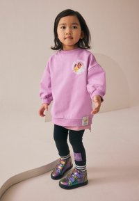 Sweatshirt rose avec un motif rond mettant en vedette des personnages, associé à un legging noir et des bottes à velcro iridescentes. Détail rayé simple au niveau de l'ourlet.
