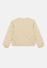 Beige tűzött, hosszú ujjú dzseki hullámos varrásmintával, kerek nyakkivágással és enyhén puffos hatással fehér háttérrel.