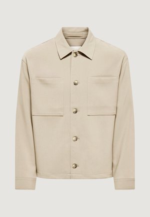 Veste beige boutonnée avec deux grandes poches poitrine, manches longues et col classique, présentée sur un fond uni.