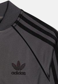 Adidas grå sporttröja med rippad krage, svarta randiga detaljer på axlarna och en liten svart logotyp på bröstet.