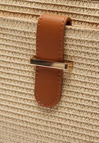 Borsa a trama beige chiaro con una tracolla in pelle marrone fissata da una chiusura orizzontale in metallo dorato.