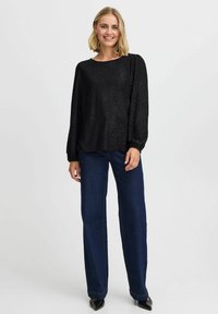 Schwarz strukturierte Bluse mit langen Ärmeln, kombiniert mit dunkelblauen weitem Jeans. Die Schuhe haben spitze schwarze Spitzen. Einfaches und lässiges Design.