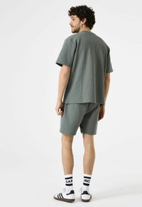 Lichtgroen, geribbeld shirt met korte mouwen en bijpassende korte broek. Materiaal lijkt textuur te hebben, met een ontspannen pasvorm. Draagt een combinatie van wit en zwarte gestreepte sokken en sneakers.