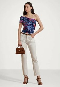 Top floral assimétrico em azul com detalhes em vermelho e rosa; jeans brancos justos; cinto castanho; bolsa castanha pequena; sandálias de salto alto castanhas.