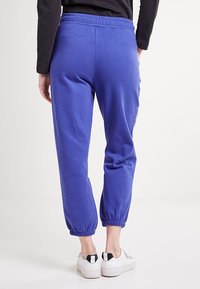 Blauwe joggers met een elastische tailleband, taps toelopende boorden en zachte stof. Ze hebben een gladde textuur en minimale detailing. Gecombineerd met witte sneakers.