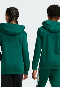 Sudadera verde con capucha, de corte relajado, mangas largas y textura lisa. Presenta detalles de costura visibles y dobladillo acanalado.