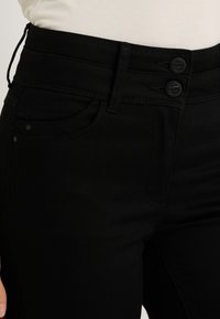 Jean noir taille haute avec une fermeture à deux boutons, des poches avant et une texture lisse. Fabriqué en denim avec une légère élasticité.