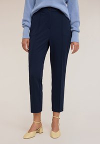 Námořnické kalhoty na míru s úzkým střihem, které mají jedno knoflíkové zapínání a přední kapsy, spárované se světle žlutými botami na blokovém podpatku.