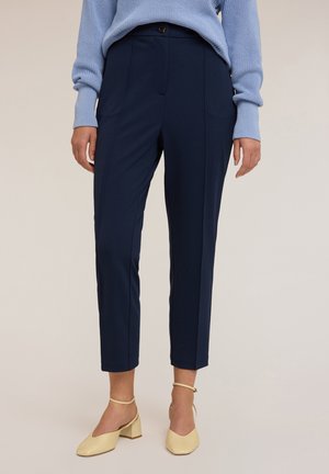 Marineblauwe op maat gemaakte broek met een slim fit, met een enkele knoopsluiting en zijzakken, gecombineerd met lichtgele blokhak schoenen.