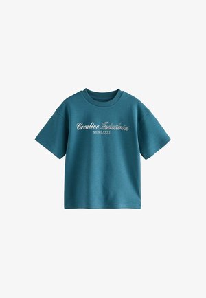 Tricou verde teal cu mâneci scurte și guler rotund, cu inscripția albă „Creative Industries MCMLXXXII” scrisă cursiv pe piept.