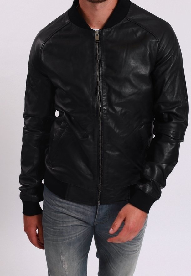 Man som bär en svart läderjacka med dragkedja, ribbade ärmslut och krage, i kombination med bleka blå jeans med slitningar.