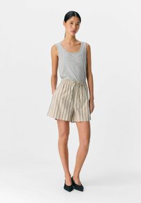 Grå ärmlös linne topp som matchas med randiga beige shorts med elastiskt midjeband och snörning; modellen bär svarta klackskor med blockhälar.