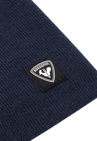 Tessuto a maglia blu navy con una toppa rettangolare nera che presenta un logo Rossignol bianco e del testo.