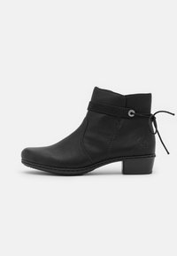 Bottine en cuir noir avec un petit talon, bout rond, bande décorative et détail de nœud sur le côté. Texture lisse et design minimaliste.
