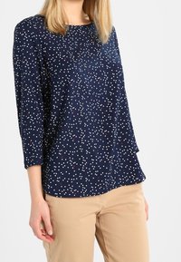 Top blu navy con maniche a tre quarti e scollo rotondo, caratterizzato da un motivo a pois bianchi e rossi distribuiti casualmente, realizzato in un tessuto liscio.