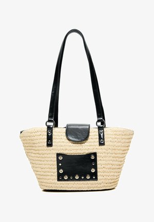 Beige gewebte Strohtasche mit langen schwarzen Griffen, einem schwarzen Lederklappverschluss und einem schwarzen, mit Nieten besetzten rechteckigen Patch vorne.