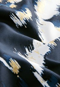 Textil s tmavomodrým základom a abstraktnými štetcovými vzormi v bielej a zlatej farbe. Tkanina má hladký, textúrovaný povrch.