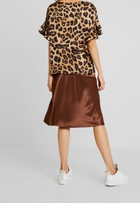 Blouse à manches courtes en imprimé léopard, associée à une jupe en satin marron arrivant aux genoux et des baskets blanches. Tissu doux avec une texture lisse.